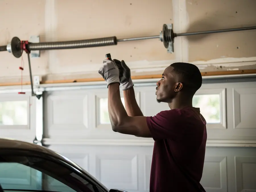 A technician in gloves works on a garage door torsion spring.