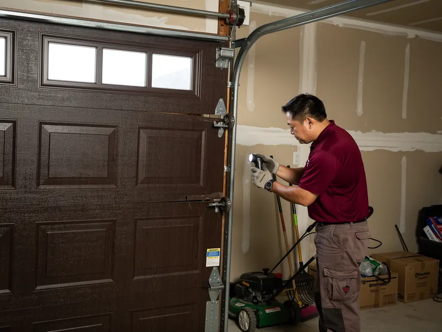 A technician shines a flashlight on a brown garage door.