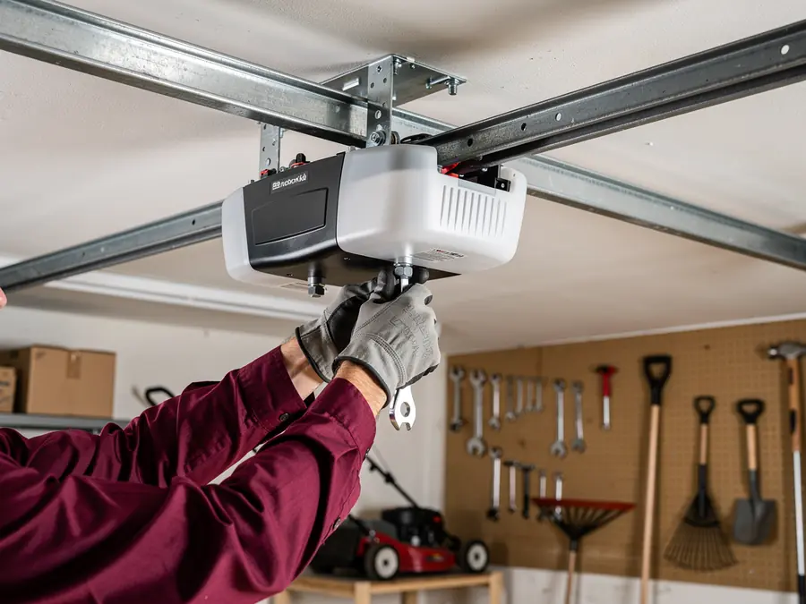 A technician in gloves is installing a garage door opener on the ceiling.